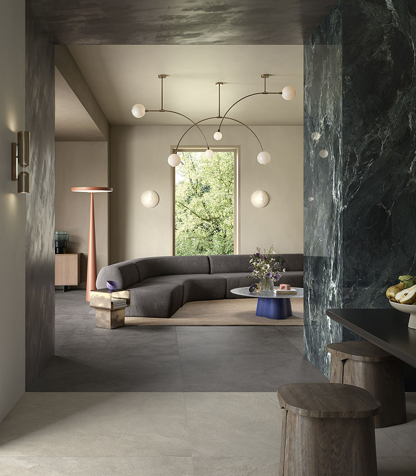 Pulse Clay und Shadow gestalten einen anspruchsvollen, materialbetonten Wohnbereich, in dem Keramikoberflächen in Steinoptik mit der ausdrucksstarken Wirkung von Noblesse Verde Alpi harmonieren.