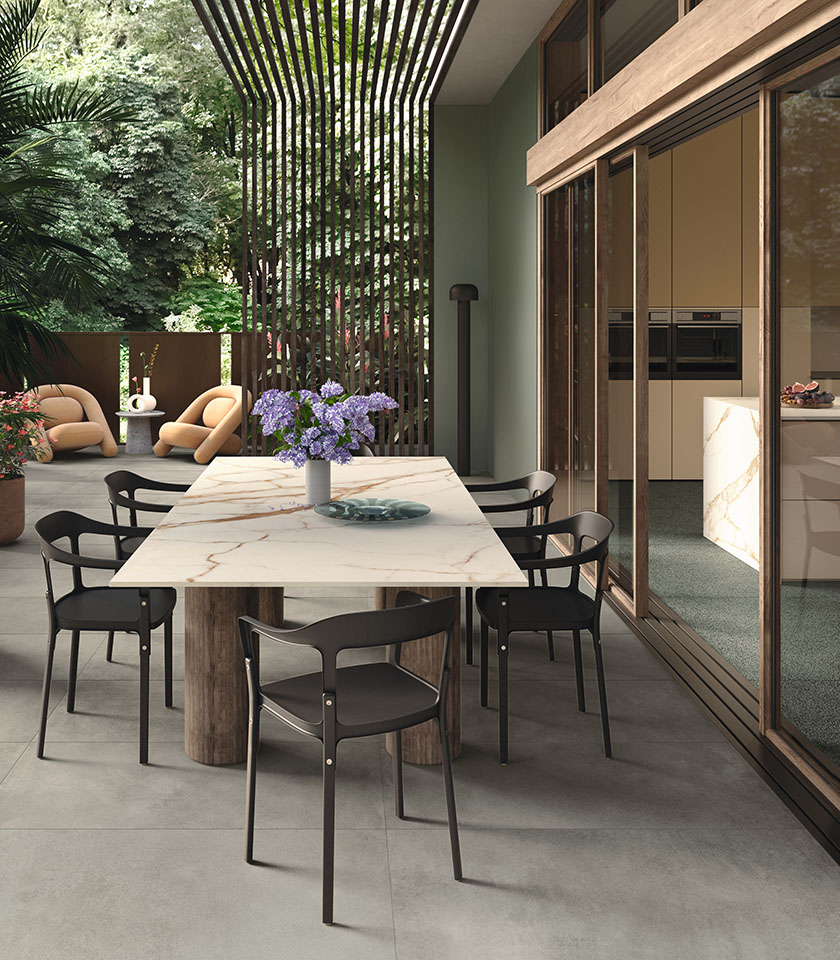 Moderner Outdoor-Essbereich mit Boden aus der Kollektion Masterpiece in Steinoptik im Farbton Master Gray, Elementen Piece Alpi und einem Tisch mit Oberfläche aus der Kollektion Delight in Marmoroptik Calacatta Oro.