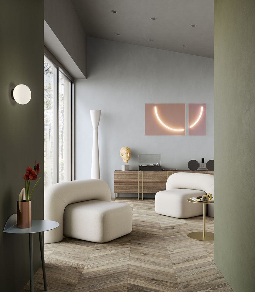 Zeitgemäßes Wohnzimmer mit Boden in Holzoptik im Fischgrätmuster, salbeigrünen Wänden, weißen Sesseln und Design-Details.