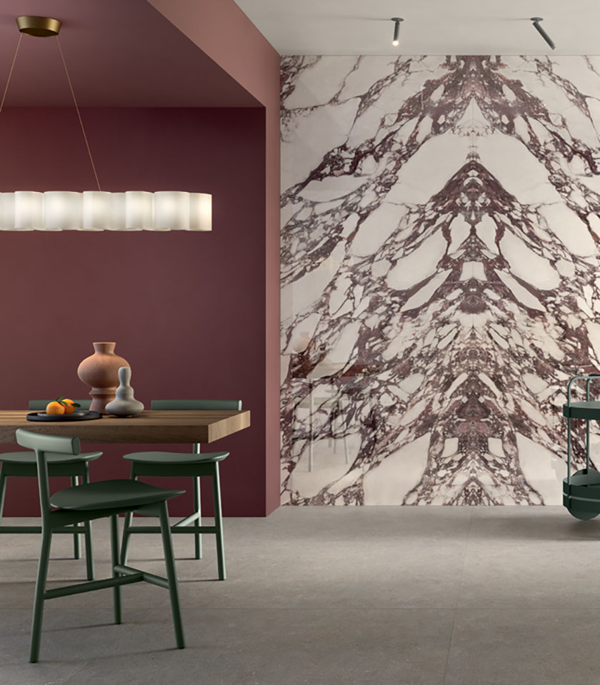 Zeitgemäßer Essbereich mit dekorativer Wand in Marmoroptik, Bordeaux-Tönen, Holztisch und grünen Stühlen.