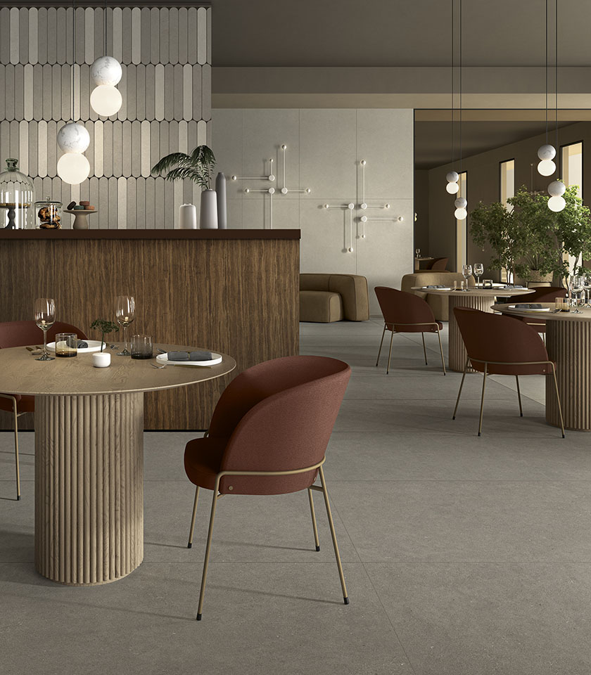 Zeitgemäßes Restaurant mit grauem Boden in Steinoptik, skulpturalen Tischen, bordeauxfarbenen Sitzmöbeln und Holzelementen.