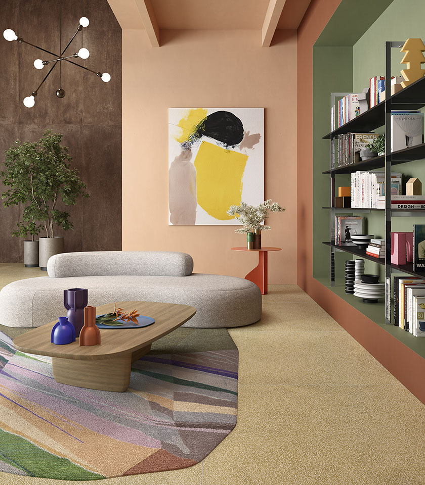 Zeitgemäßes Wohnzimmer mit beigefarbenem Boden, Wand in Betonoptik, skulpturalem Sofa und integrierter Regalwand vor grünem Hintergrund.