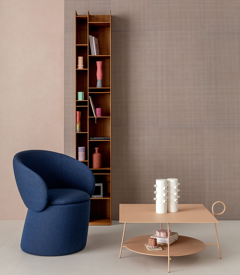 Zeitgemäßer Innenraum mit blauem Sessel, Couchtisch in Pudertönen, Holzregal und dekorativer Wand mit feinem Mikromuster.