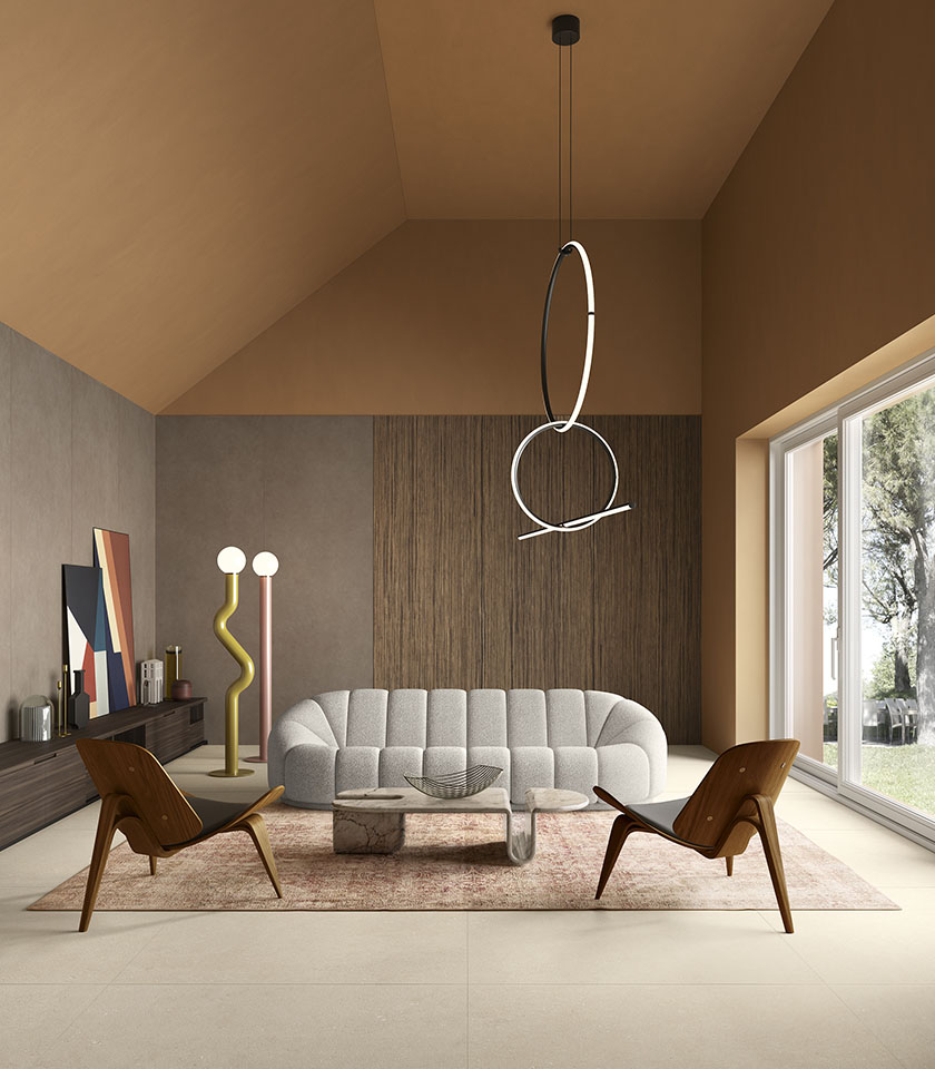 Zeitgemäßes Wohnzimmer mit beigefarbenem Boden in Steinoptik, skulpturalem Sofa, Holzsesseln und großen Fenstern mit Blick ins Grüne.