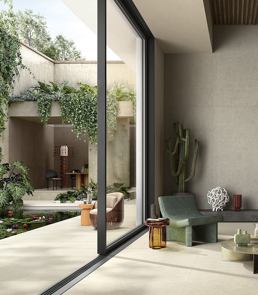 Indoor-Outdoor-Bereich mit hellem Feinsteinzeugboden, großen Glasfronten, üppiger Begrünung und modernen Möbeln.