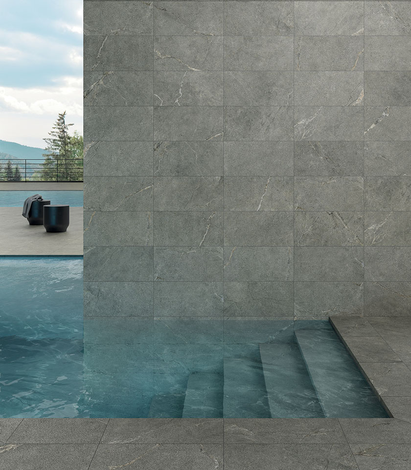 Pool mit grauen Feinsteinzeugfliesen in Steinoptik an Wand und Boden, Unterwasserstufen und Blick auf die Berge.