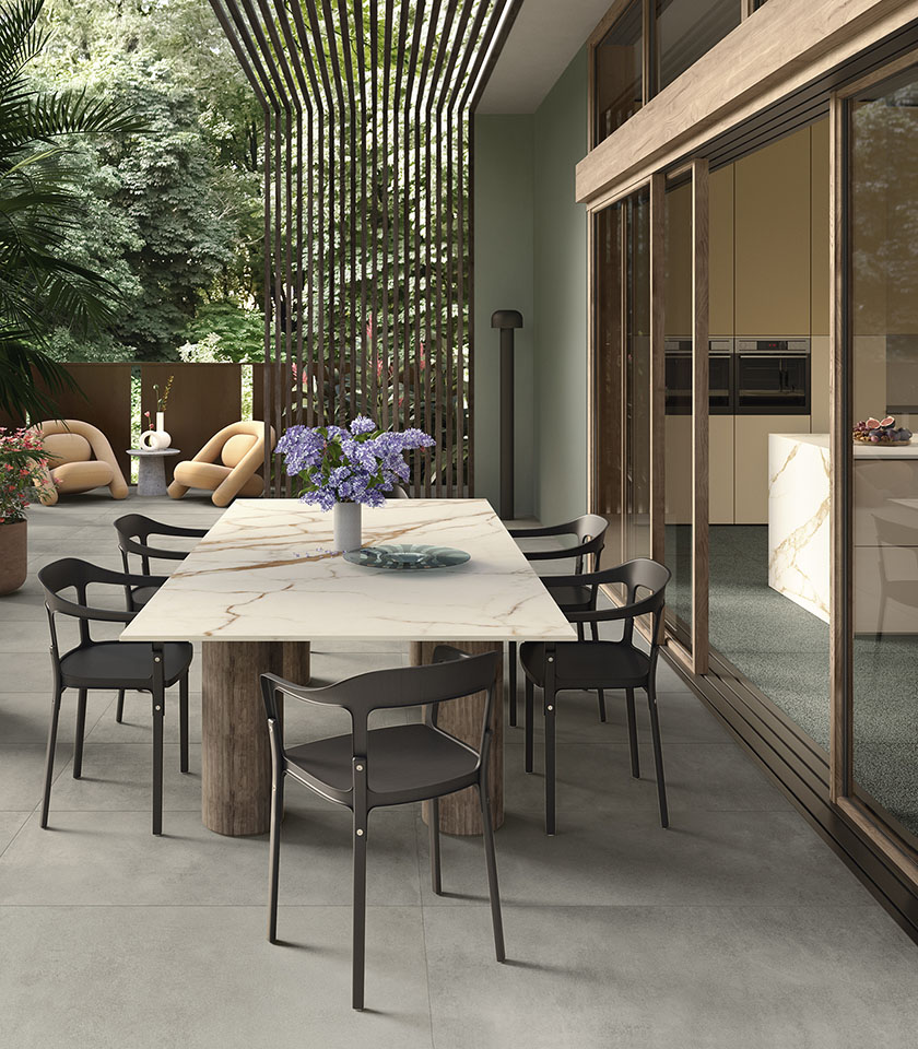 Moderne Terrasse mit Feinsteinzeugboden, Designmöbeln, großem Tisch in Marmoroptik und fließendem Übergang zwischen Innen- und Außenbereich.