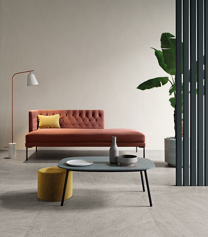 Minimal-Chic-Wohnzimmer mit grauem Boden in Steinoptik, terrakottafarbener Chaiselongue, reduzierter Einrichtung und warmen zeitgenössischen Designakzenten.