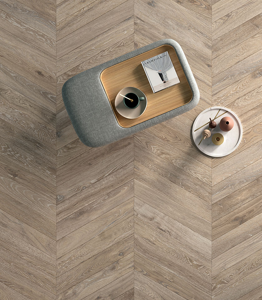 Feinsteinzeugboden in Holzoptik mit Chevron-Verlegung, von oben mit modernen Design-Tischen dargestellt.